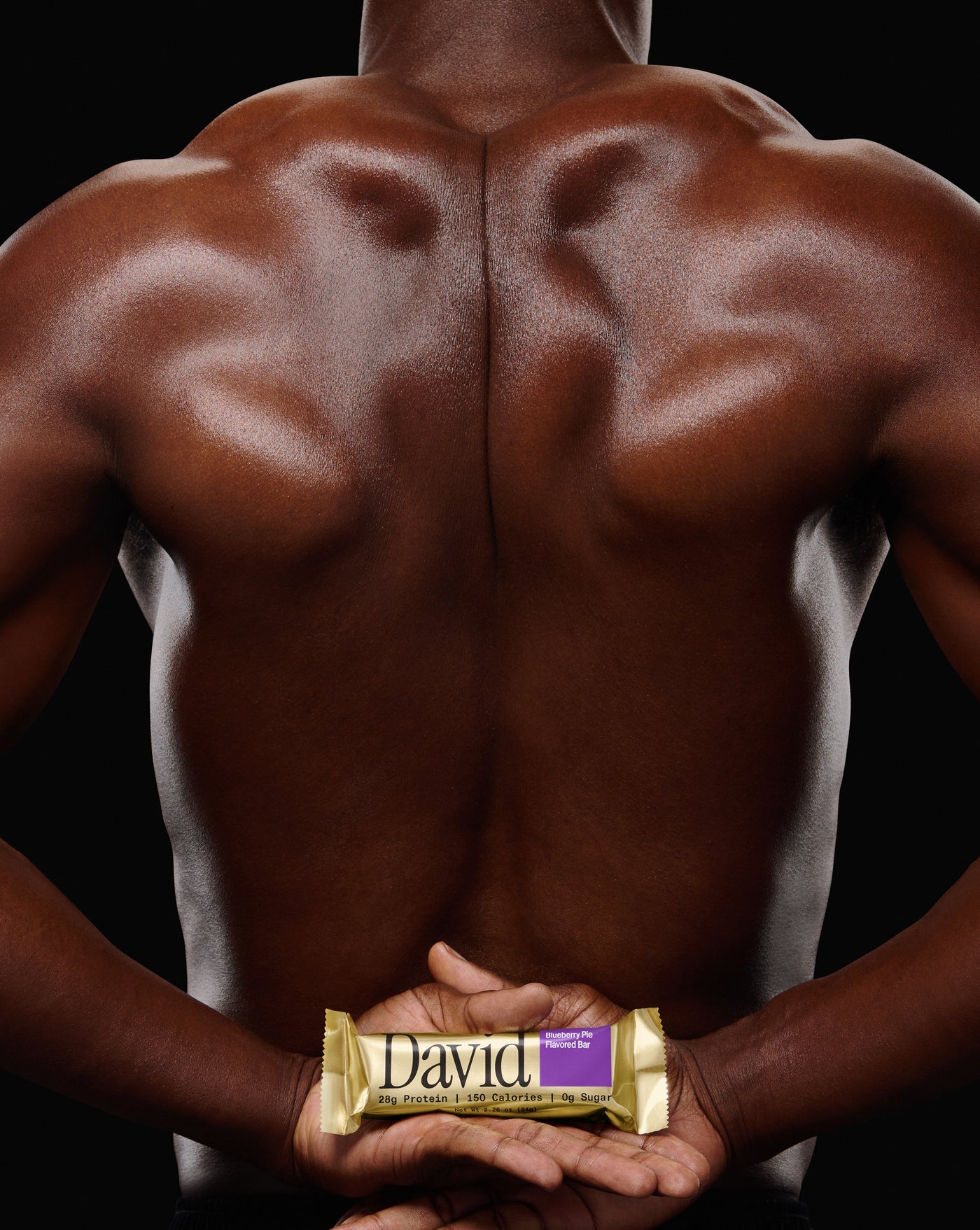 Person's back holding a David Blueberry Pie protein bar with a black background
