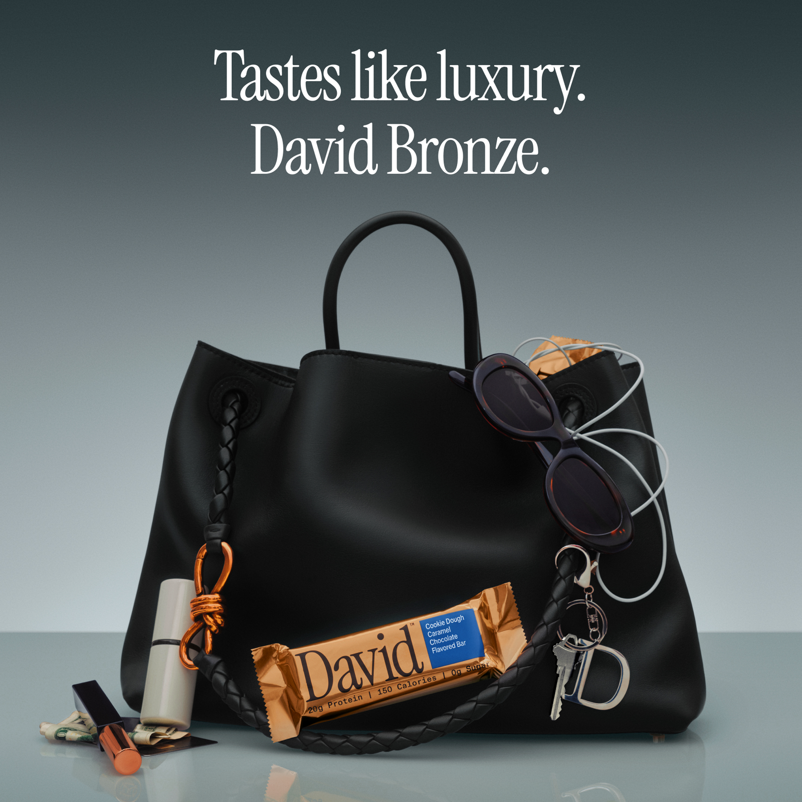 Black handbag with accessories and David Bronze protein bar on a gray background.