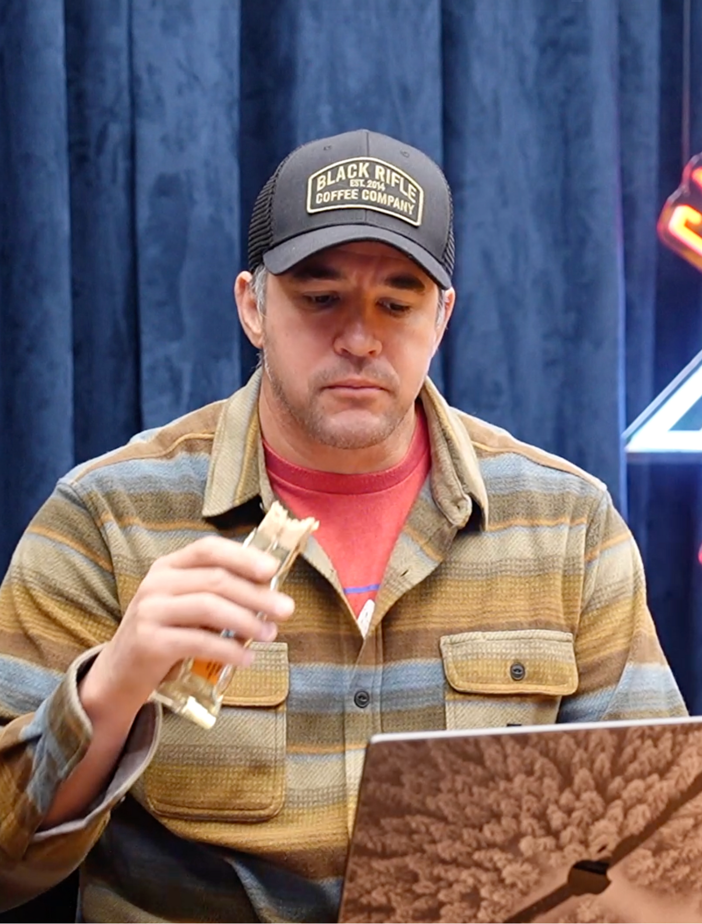 Man sitting in front of a laptop eating a David Protein Gold bar in front of a blue curtain