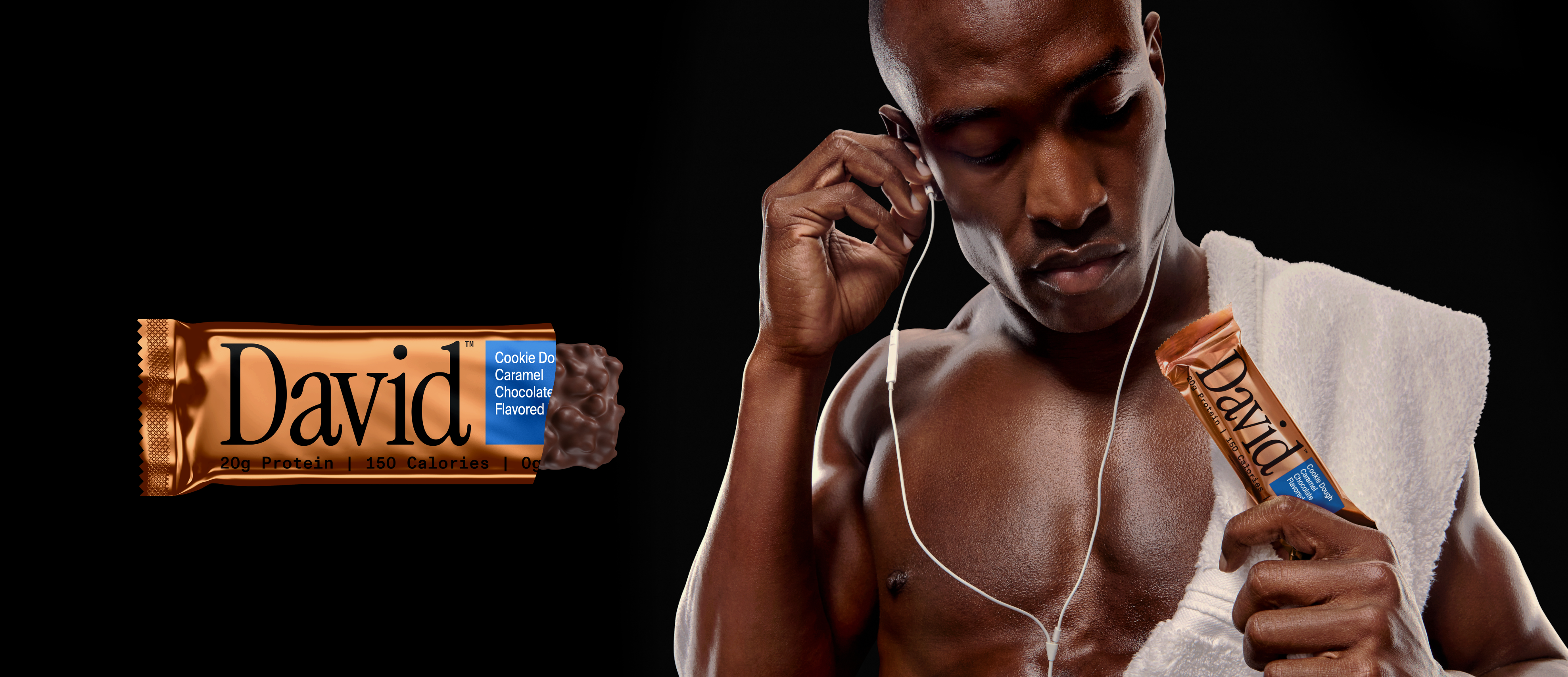 Man holding a Cookie Dough Caramel Chocolate David protein bar with headphones a dark background with a Cookie Dough Caramel Chocolate David protein bar partially unwrapped.