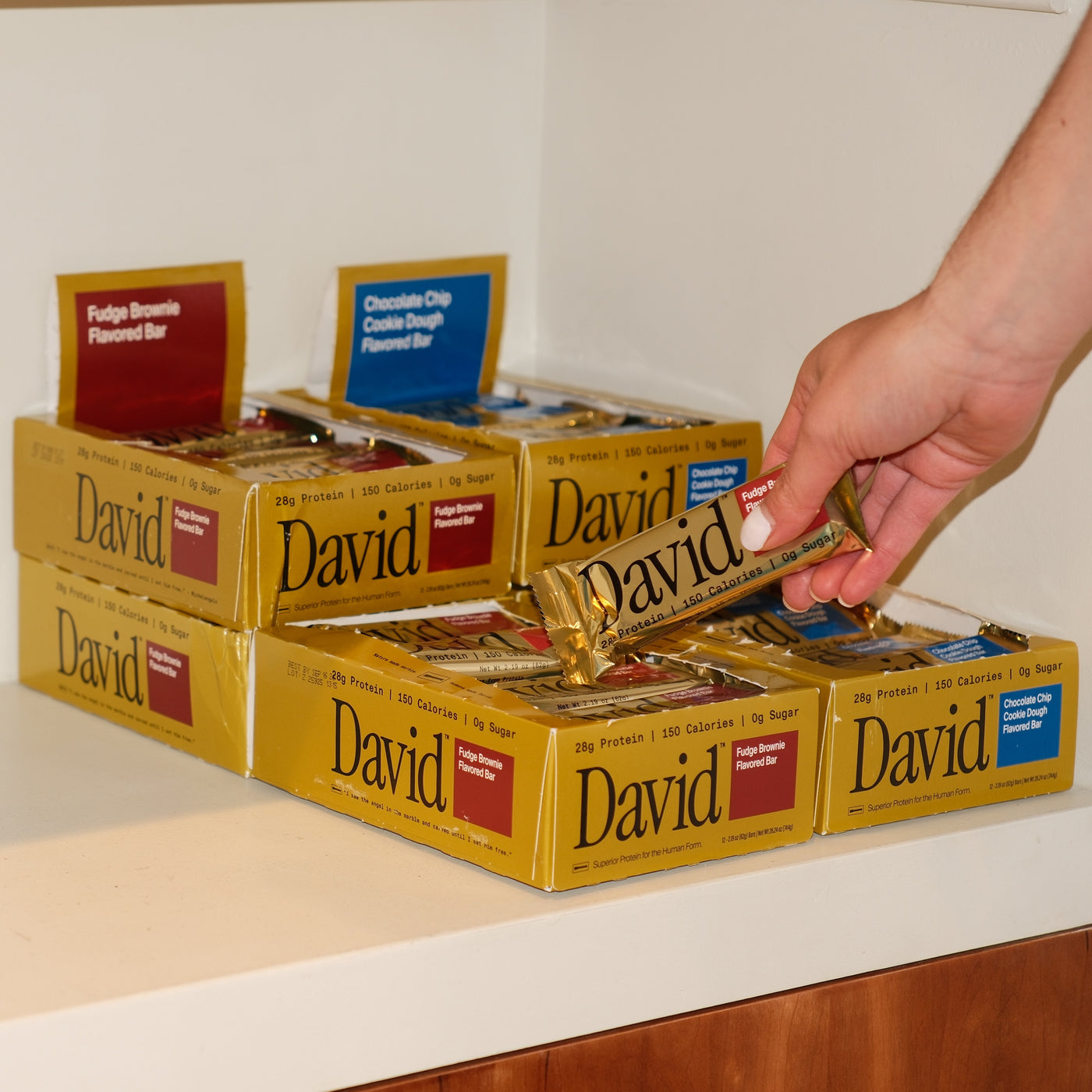 Hand picking a David protein bar from a display of the product on a counter.
