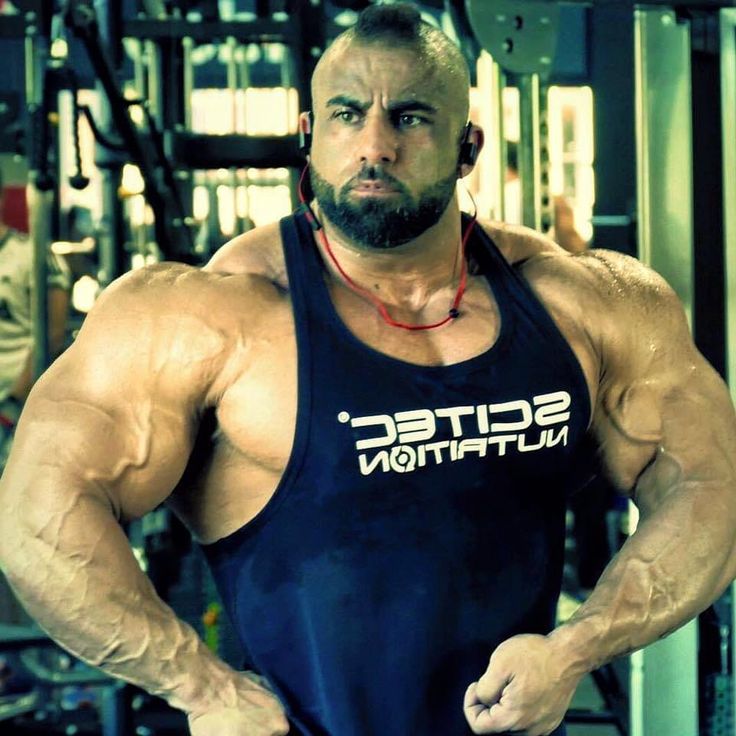 Muscular man in a gym wearing a tank top with a brand logo.