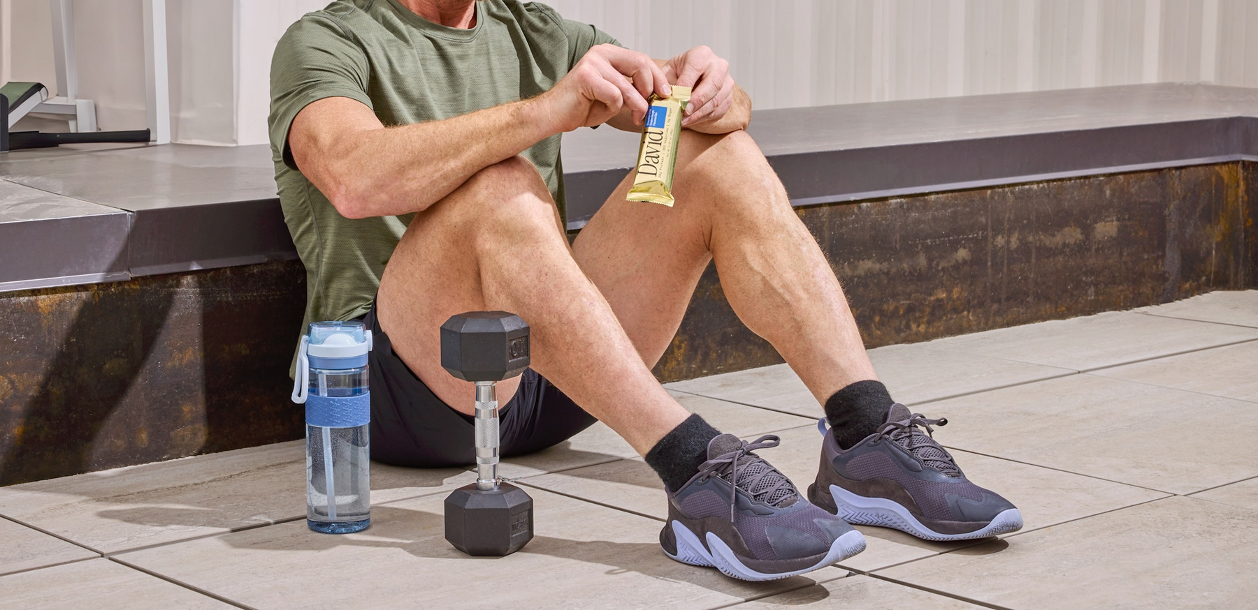 Man sitting on a floor with a David Protein Gold bar next to a weight