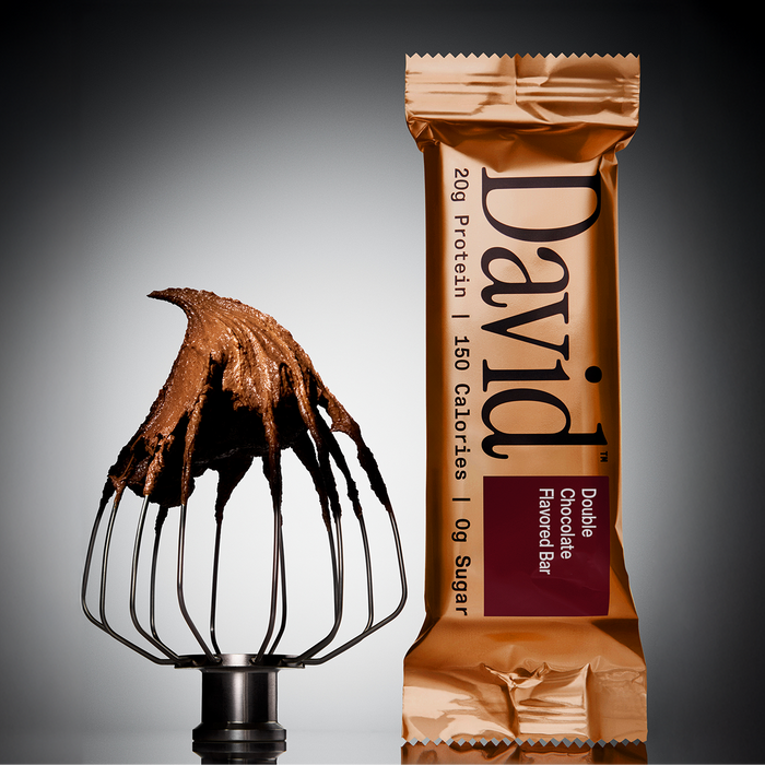 David Protein Fudge Brownie flavored high-protein bar in gold wrapper next to a whisk head coated with swirled chocolate