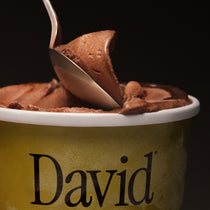 Spoon dipping into a container of chocolate ice cream branded 'David' on a black background