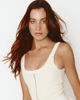 Woman wearing a white sleeveless top against a plain background