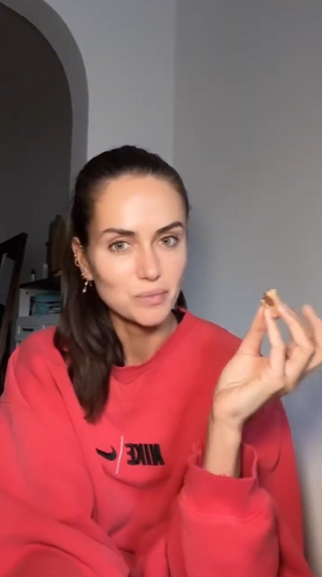 Person wearing a red sweatshirt with a brand logo, holding a bite of a David Protein bar