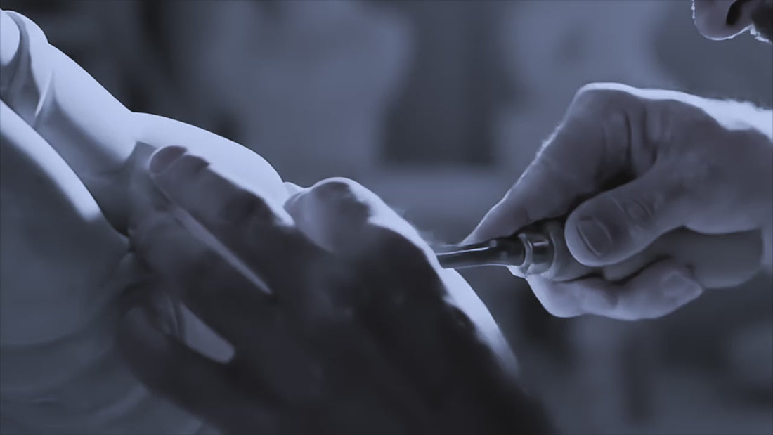 Close up video of a man with a chisel cutting into a white sculpture. 